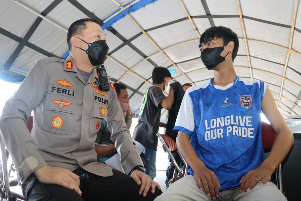 Demi Saksikan Laga Arema, Aremania Pasuruan Ikuti Vaksinasi Booster di Kanjuruhan AKBP Ferli menyapa salah satu Aremania asal Pasuruan yang mengikuti vaksinasi di lobi Stadion Kanjuruhan